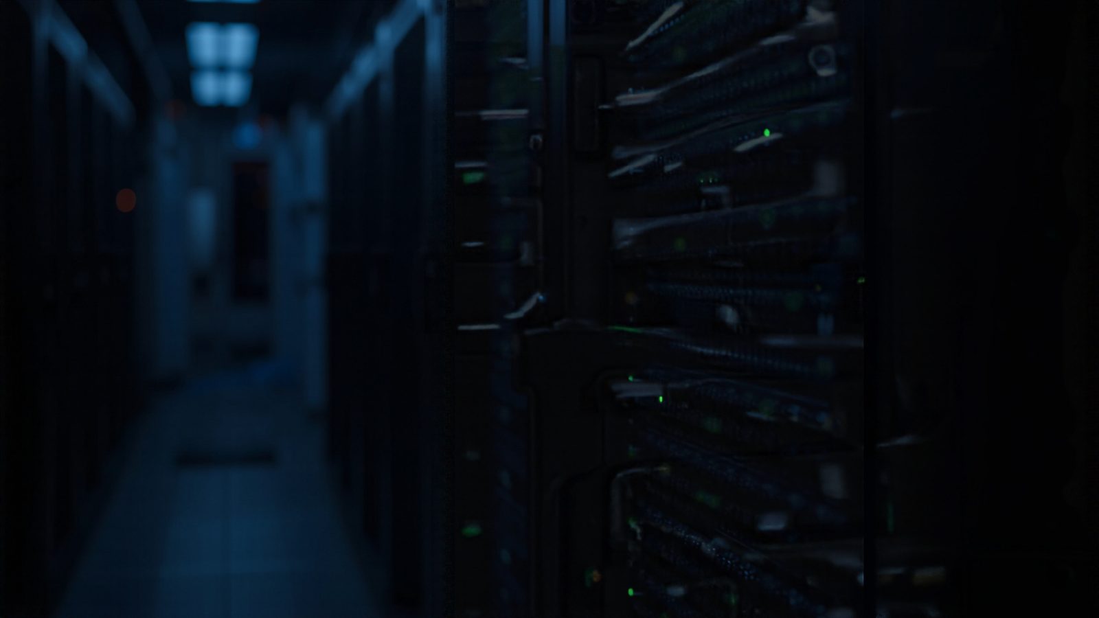 A dim server room with a dark equipment rack and small glowing indicator lights, shallow depth of field.